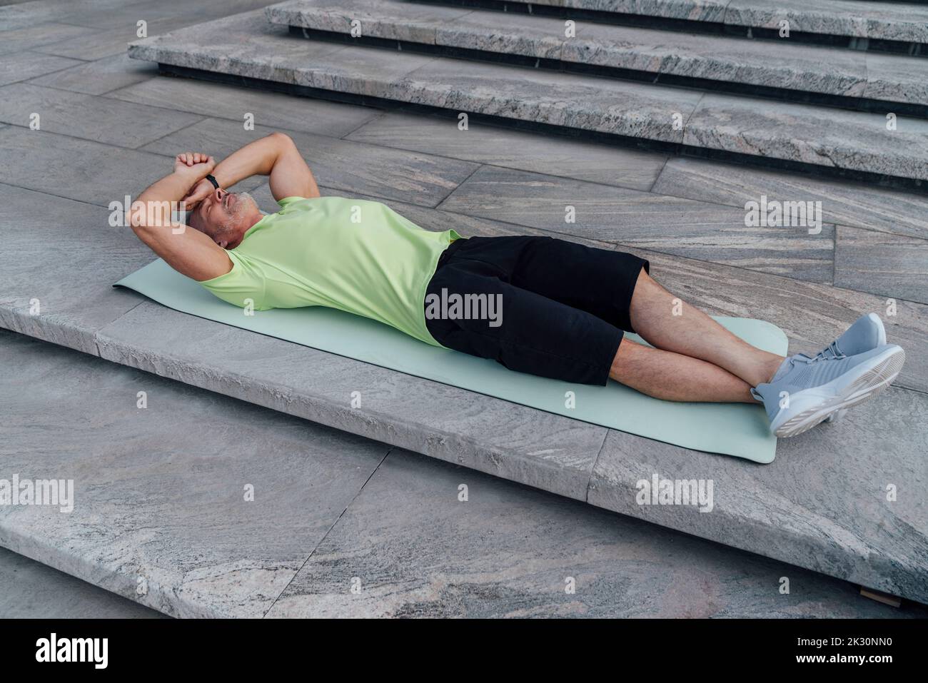 Müder Mann, der auf einer Yogamatte in der Nähe der Stufen liegt Stockfoto