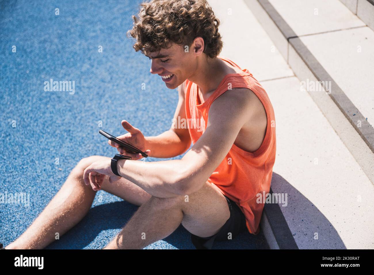 Glücklicher Sportler mit Smartphone vor der Treppe sitzen Stockfoto