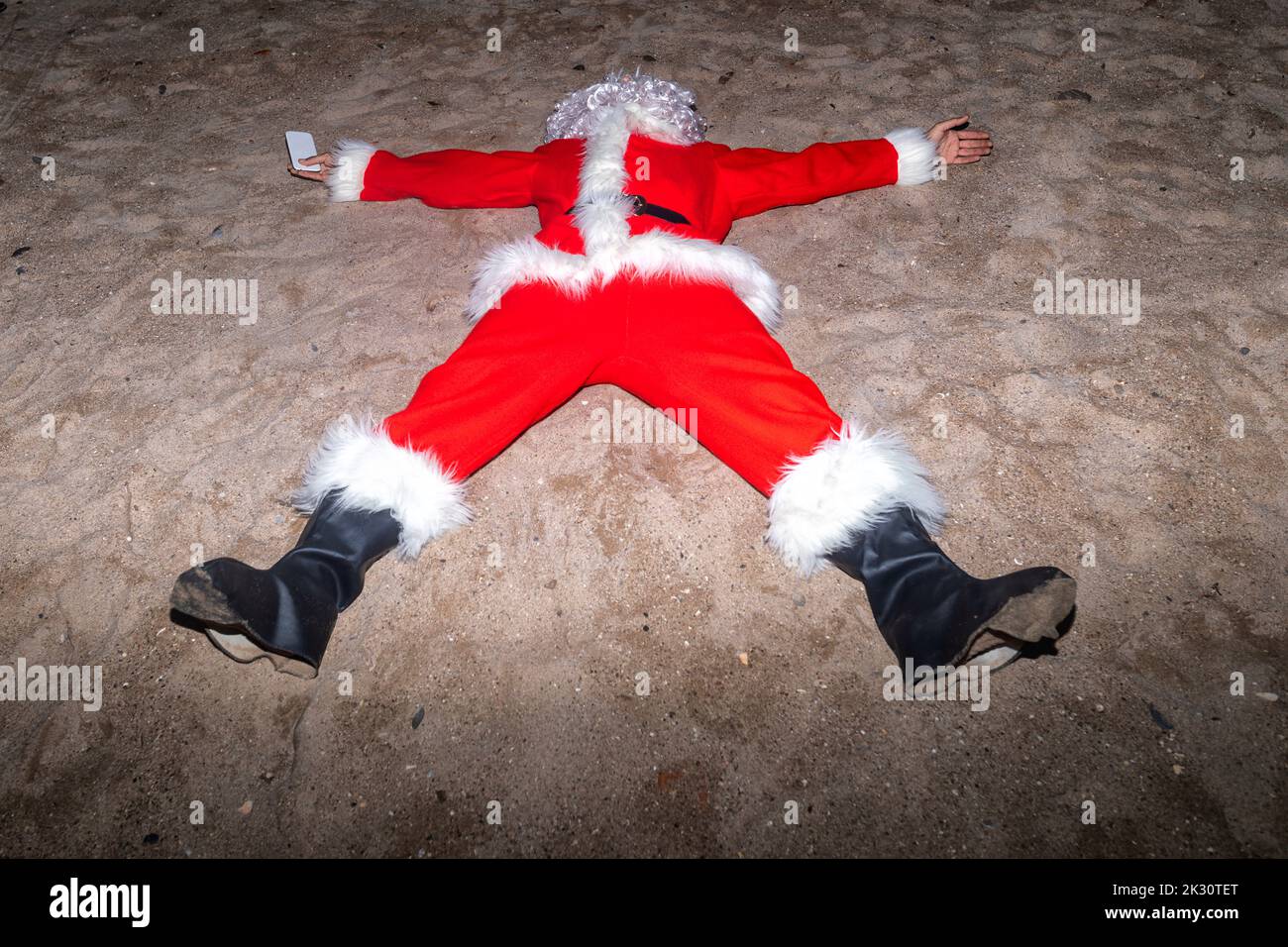 Mann im Weihnachtsmann-Kostüm, der am Strand auf Sand liegt Stockfoto