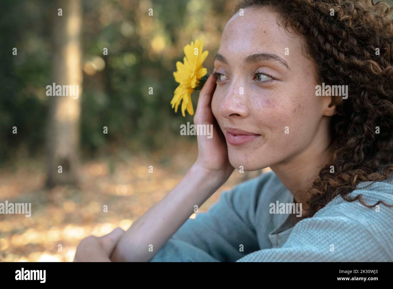 Nachdenkliche junge Frau mit gelber Blume im Park Stockfoto