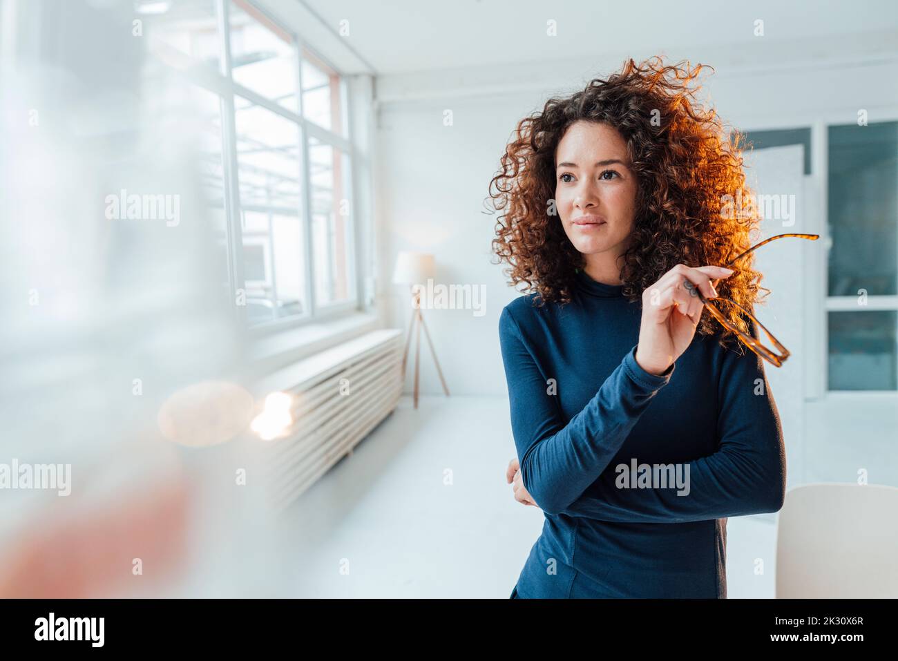 Eine durchdachte Geschäftsfrau mit lockigen Haaren und einer Brille Stockfoto
