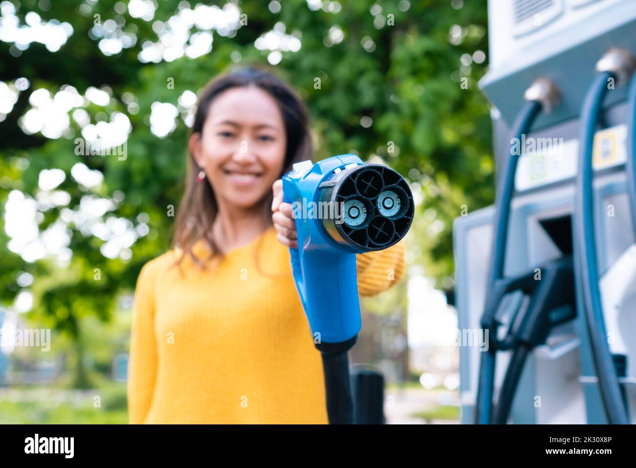 Frau zeigt das Ladekabel an der elektrischen Ladestation Stockfoto