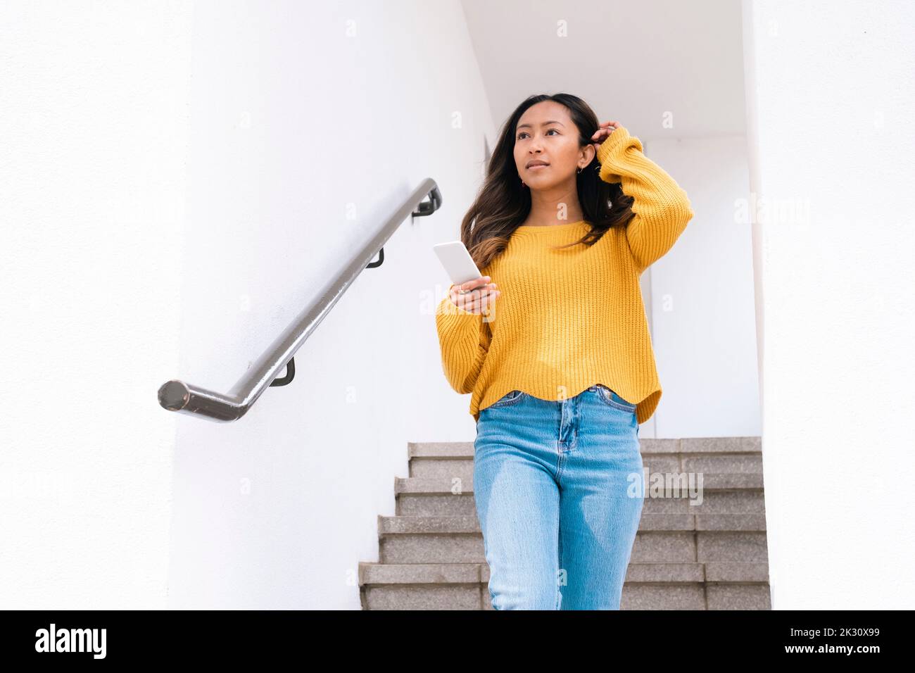 Nachdenkliche junge Frau mit Mobiltelefon, das sich auf Stufen nach unten bewegt Stockfoto