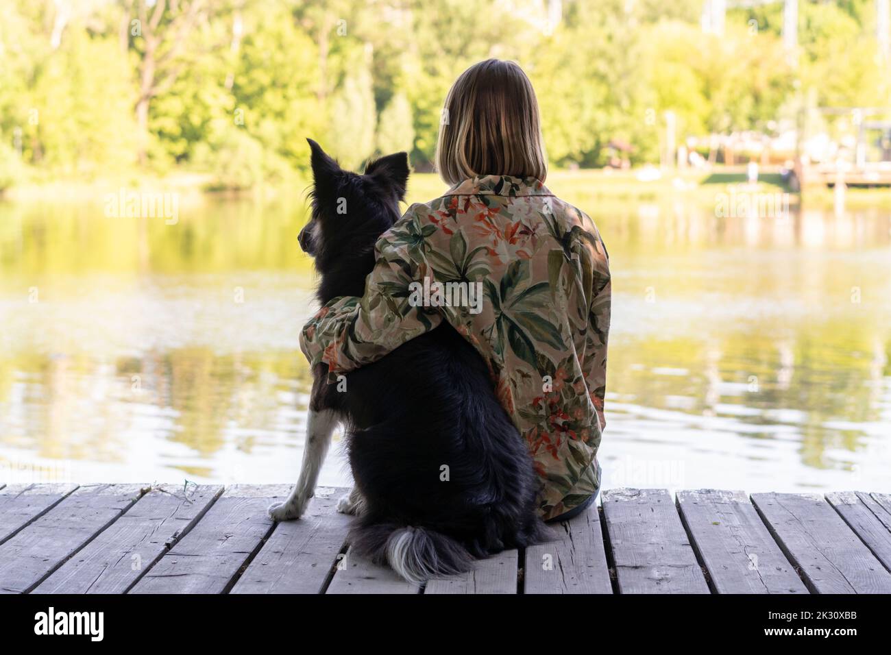 Junge Frau, die mit Hund am See im Park sitzt Stockfoto