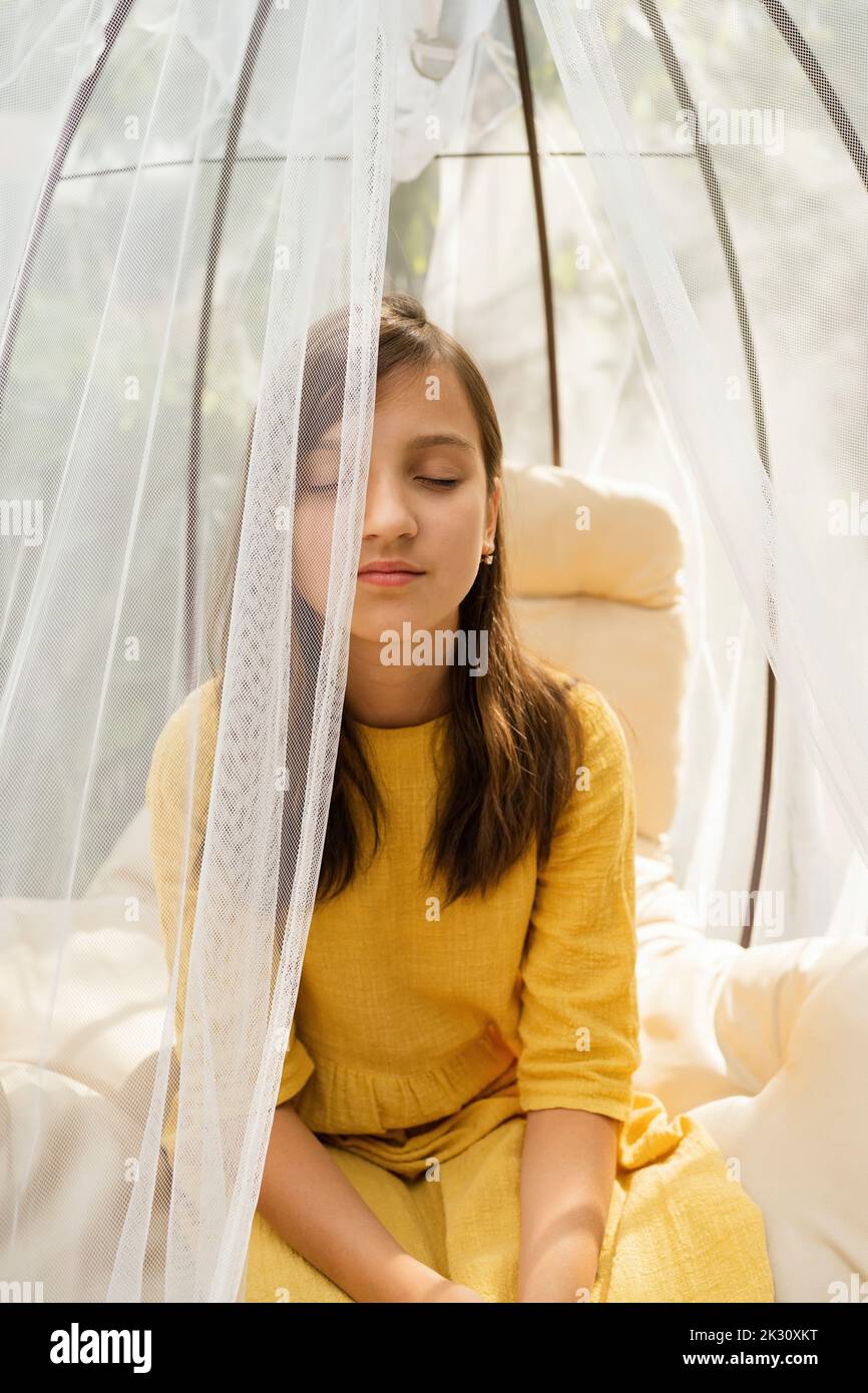 Vorpubertär Mädchen mit geschlossenen Augen sitzen in hängenden Stuhl Stockfoto