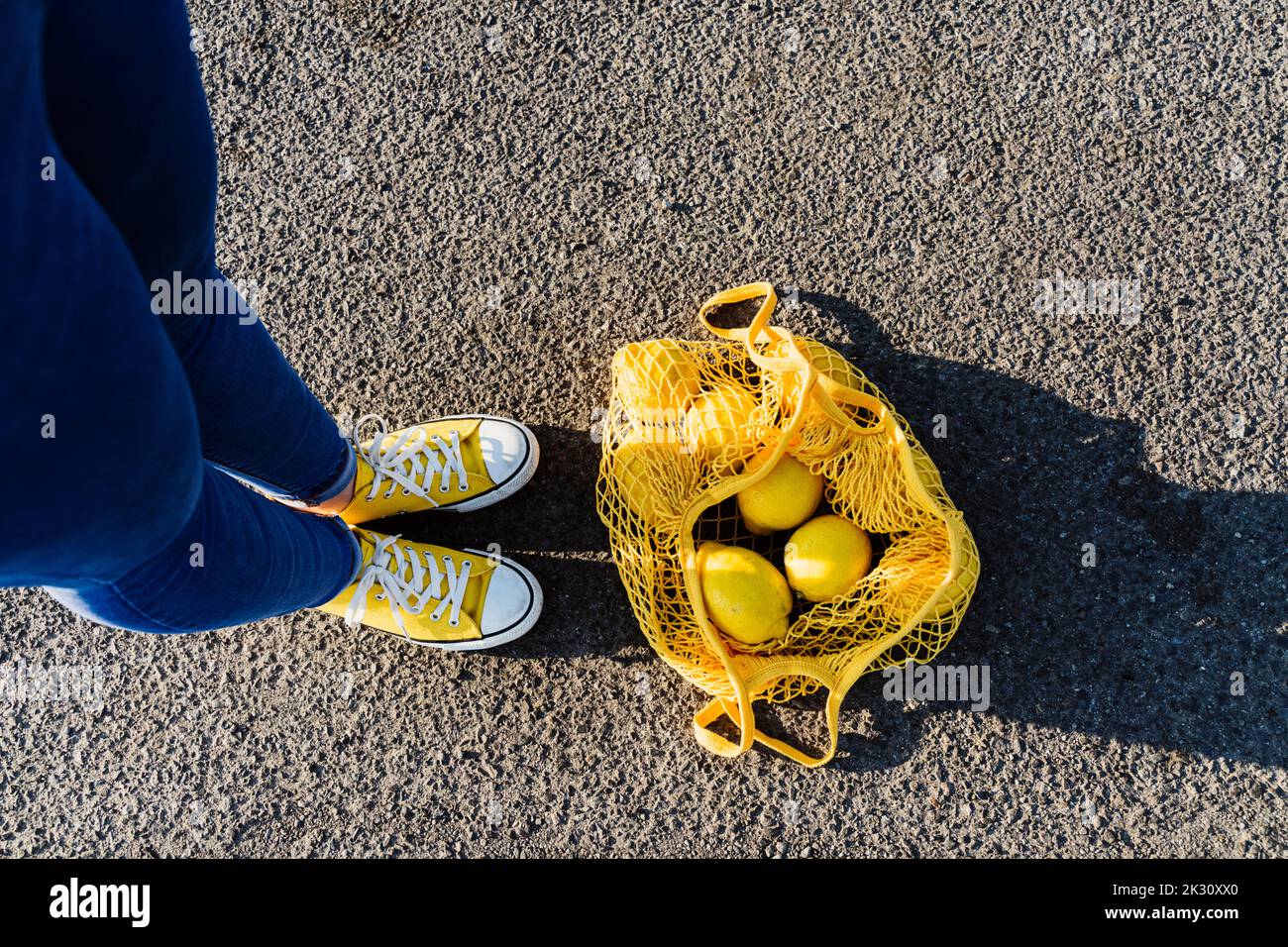 Frau, die auf Asphalt durch einen Netzbeutel mit Zitronen steht Stockfoto