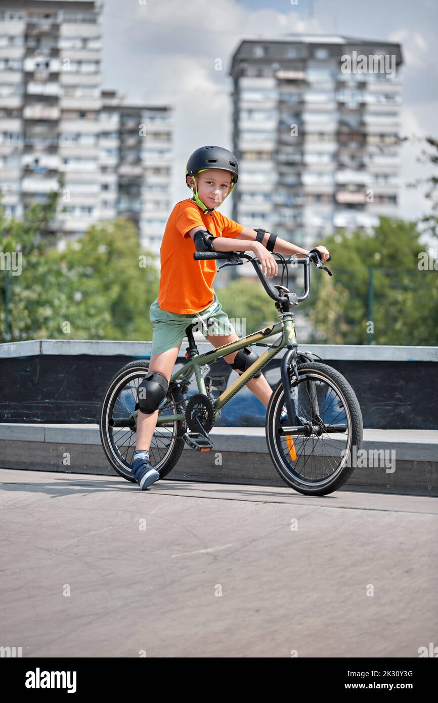 Boy mit Sicherheitsausrüstung sitzt auf BMX-Fahrrad im Skateboard Park Stockfoto