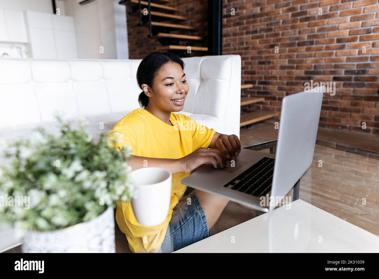 Frau, die im Wohnzimmer sitzt und von zu Hause aus mit einem Laptop arbeitet Stockfoto