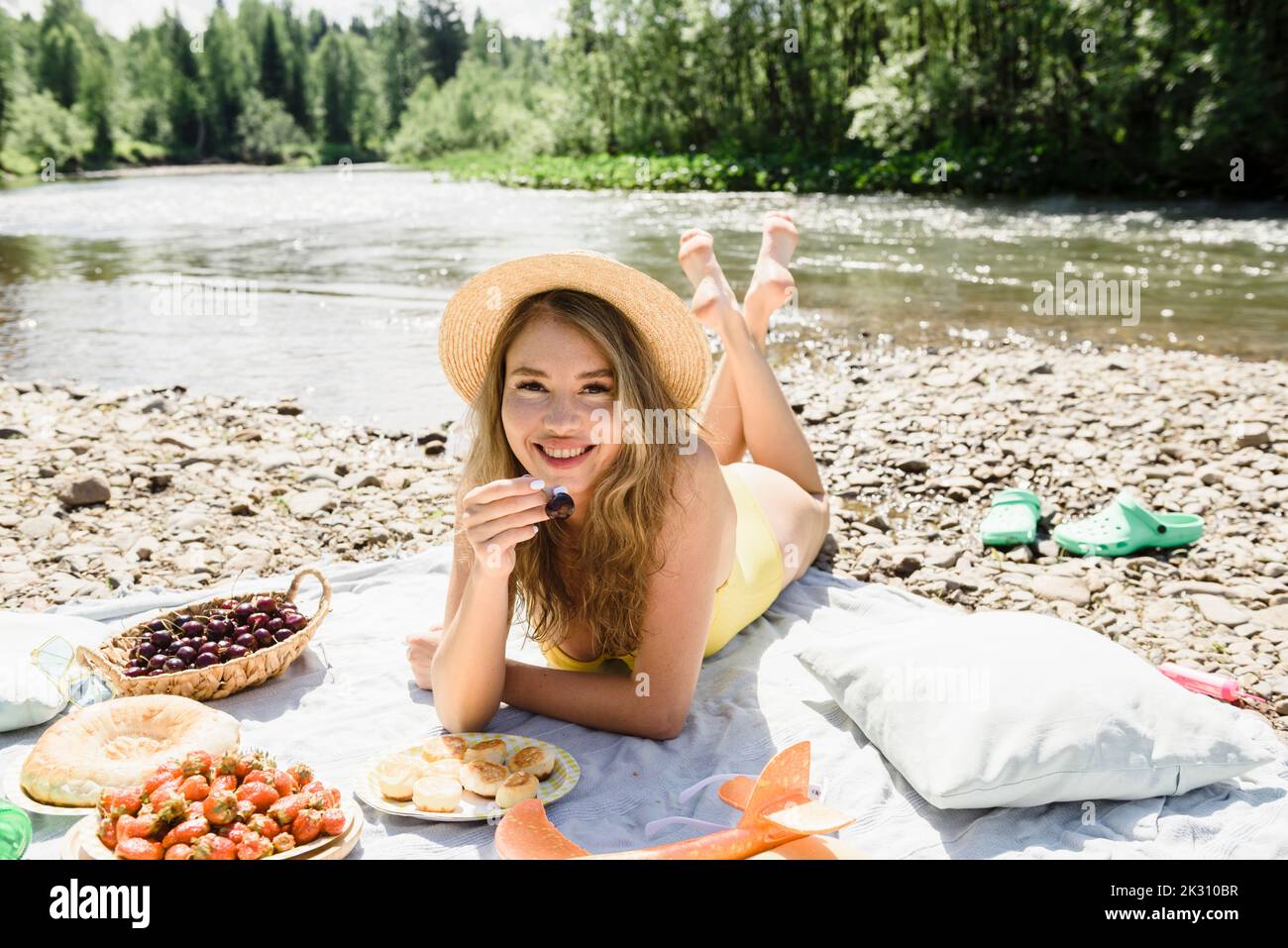 Frau mit Kirsche auf der Decke am Flussufer liegend Stockfoto