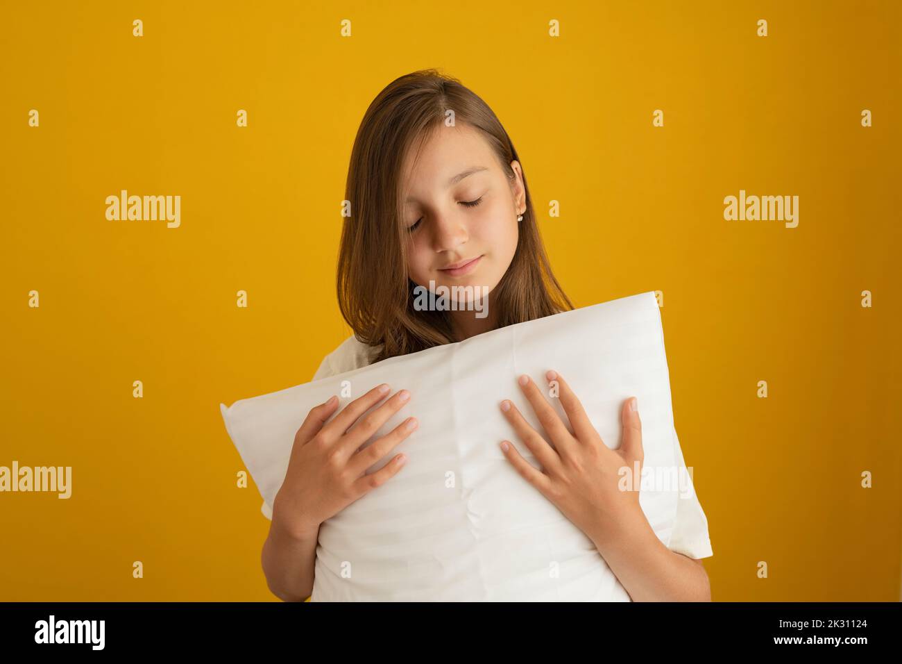 Mädchen mit geschlossenen Augen hält weißes Kissen vor gelbem Hintergrund Stockfoto