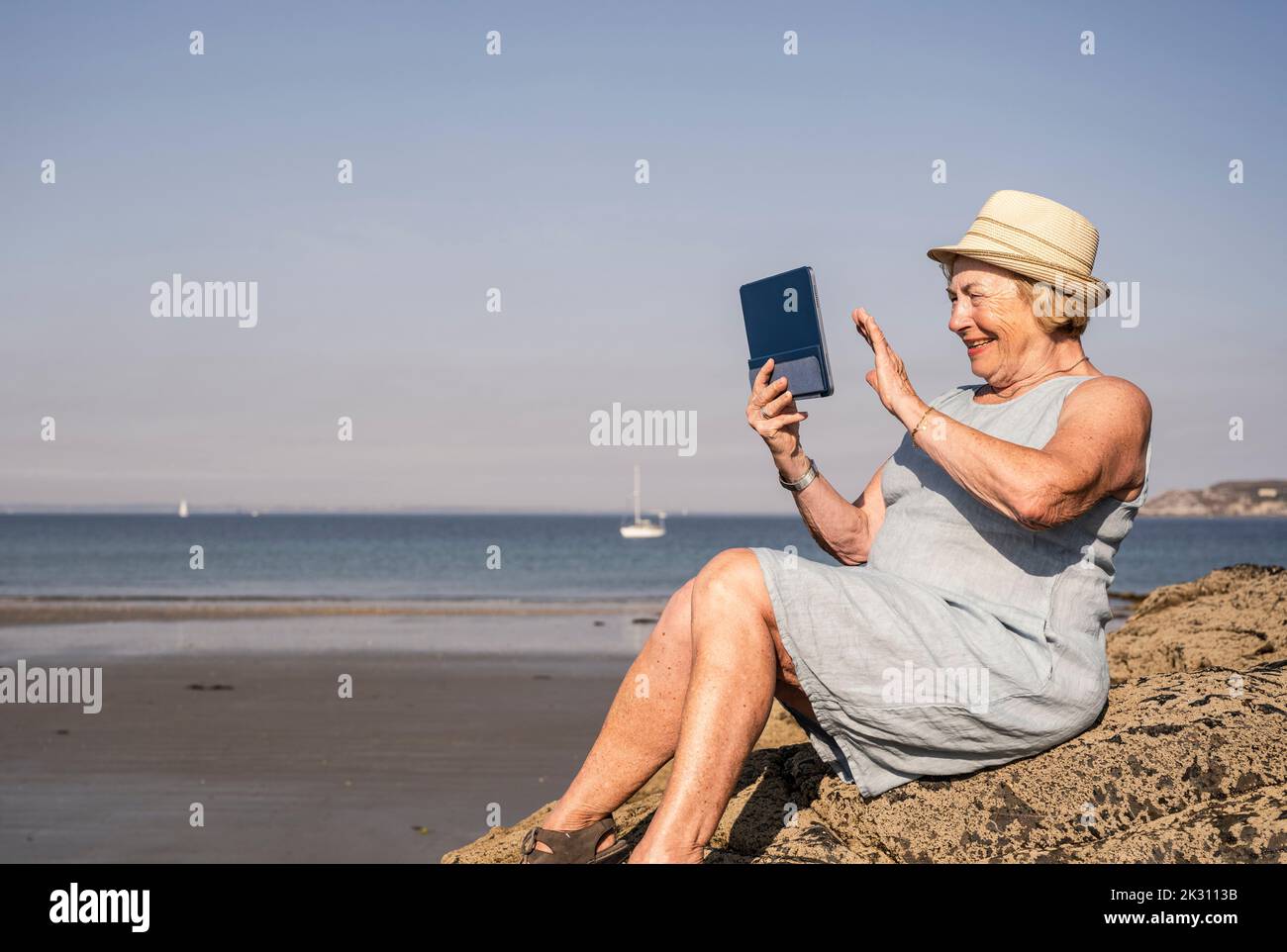 Glückliche ältere Frau, die beim Videoanruf am Strand mit der Hand winkt Stockfoto