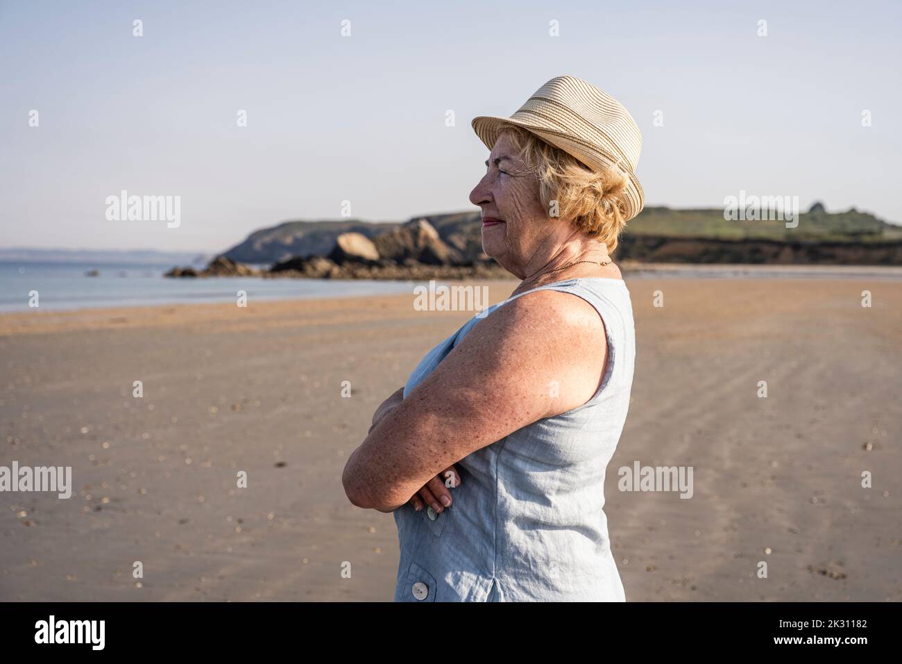 Ältere Frau mit gekreuzten Armen, die am Strand steht Stockfoto
