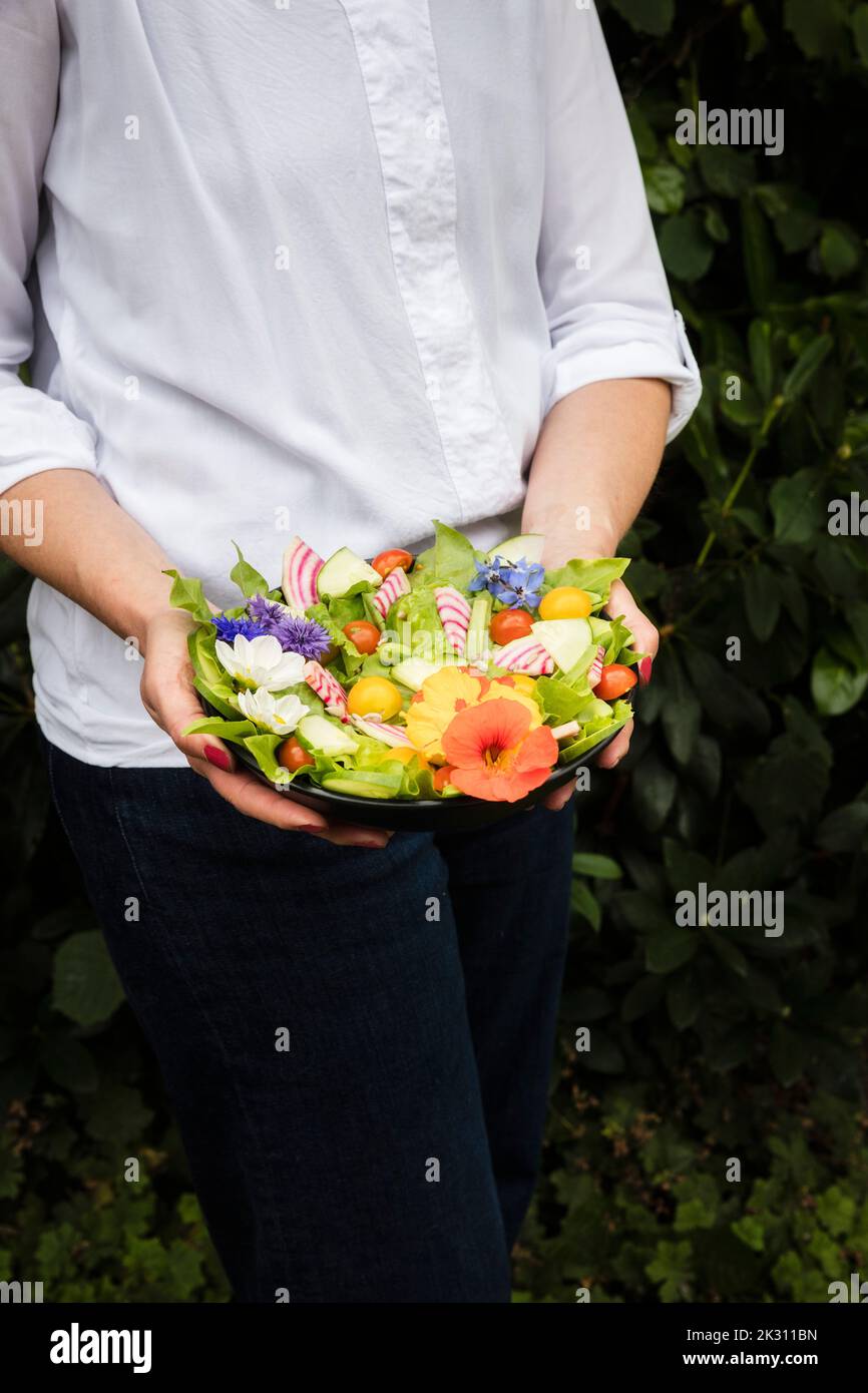 Mittelteil der Frau, die eine Schüssel mit veganem Salat mit Gemüse und essbaren Blumen hält Stockfoto