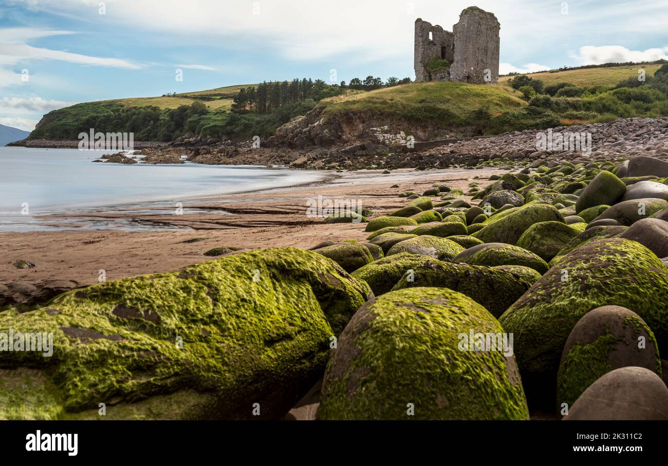 Irland, Kilmurry, Felsbrocken am Strand mit alter Ruine im Hintergrund Stockfoto