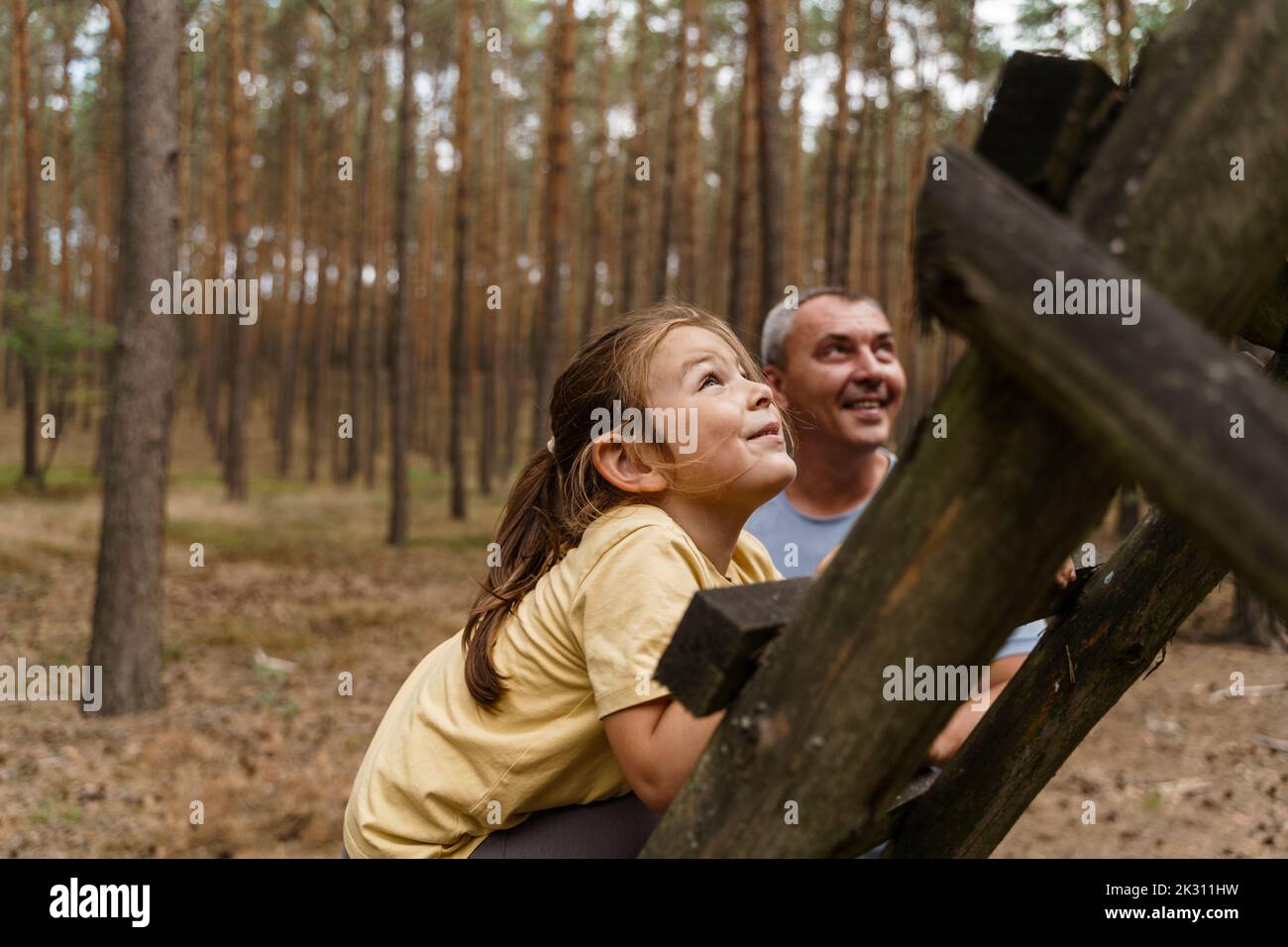 Lächelndes Mädchen klettert Leiter im Wald Stockfoto