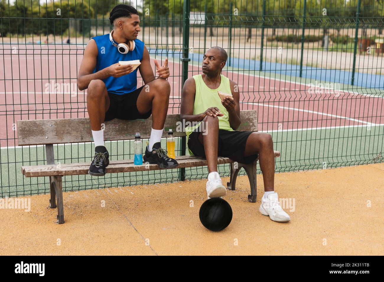 Vater und Sohn essen Sandwiches auf der Bank am Basketballplatz Stockfoto
