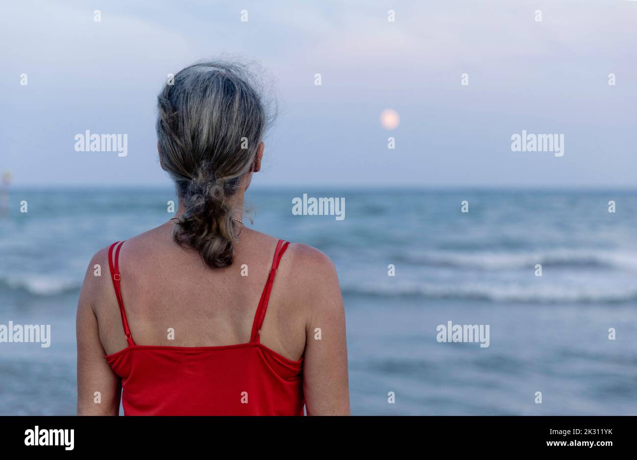 Frau mit grauem Haar, die den Mond über dem Horizont betrachtet Stockfoto