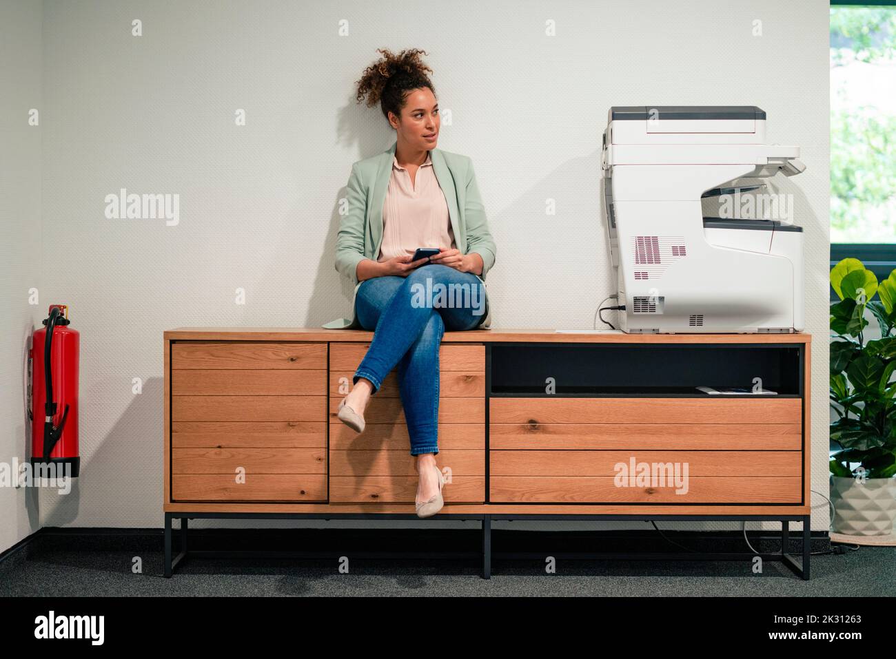Kontemplative Geschäftsfrau, die im Büro auf einem Beistelltisch sitzt Stockfoto
