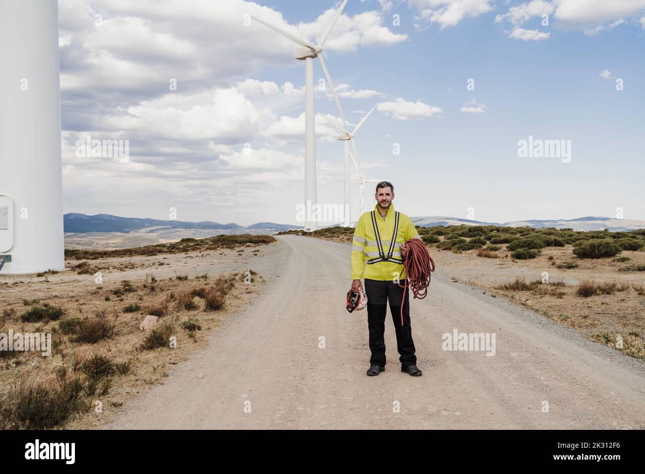 Ingenieur mit Helm und Seil, der auf der Straße im Windpark steht Stockfoto