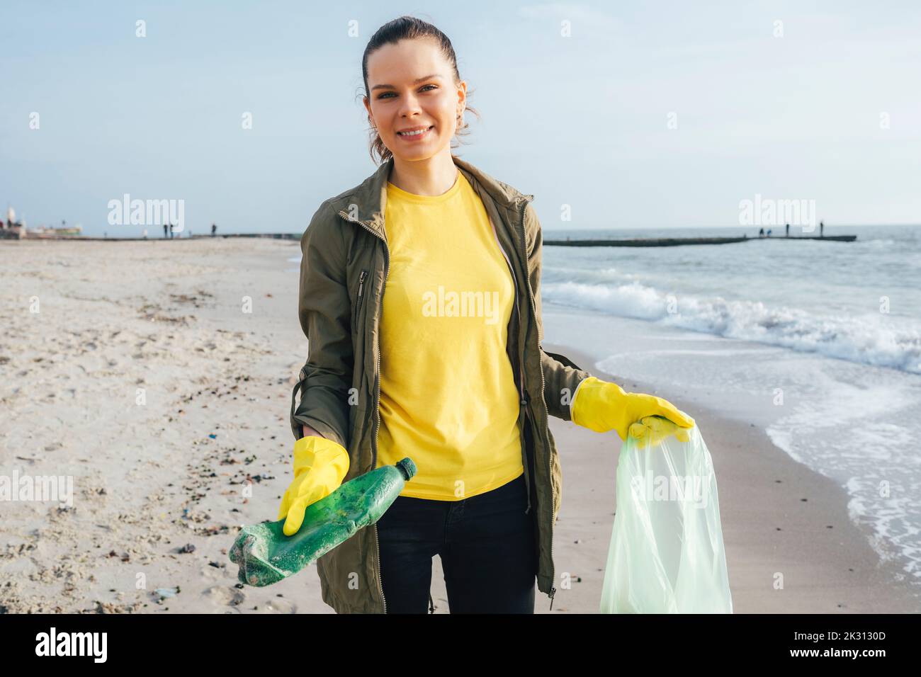 Lächelnder Freiwilliger sammelt Plastikmüll in Mülltüten am Strand Stockfoto