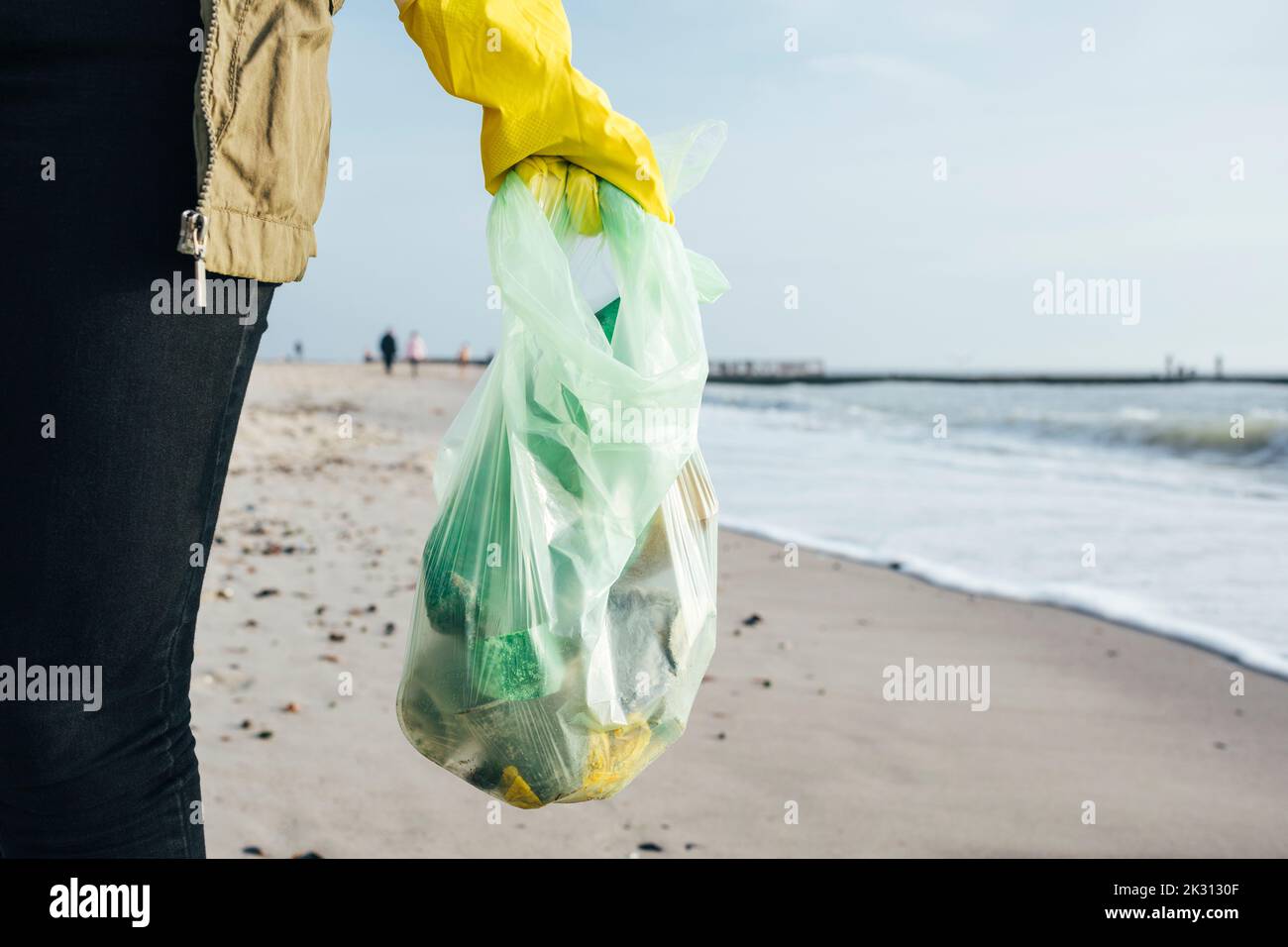 Hand einer Frau, die am Strand einen Müllbeutel mit Plastikmüll hält Stockfoto