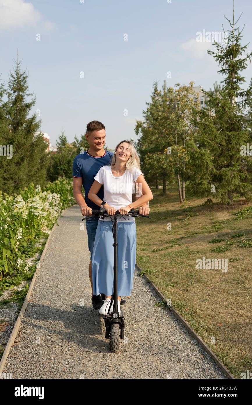 Junge Frau mit Freund genießen Elektroroller Fahrt im Park Stockfoto