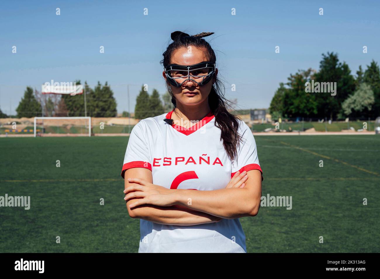 Der Spieler trägt eine Schutzbrille und steht mit gekreuzten Armen auf dem Lacrosse-Feld Stockfoto