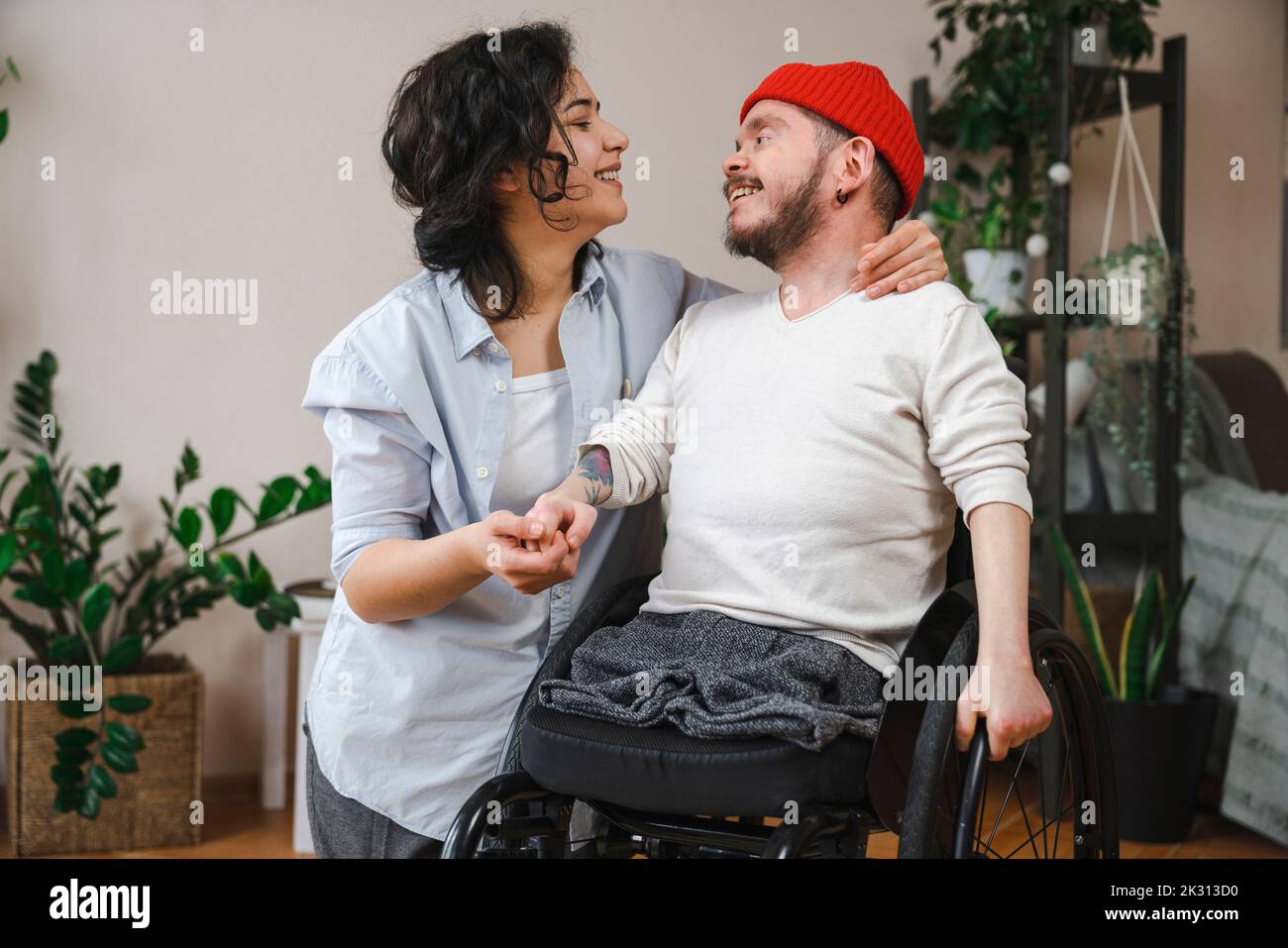Lächelnder Mann im Rollstuhl, der die Hand der Freundin zu Hause hält Stockfoto