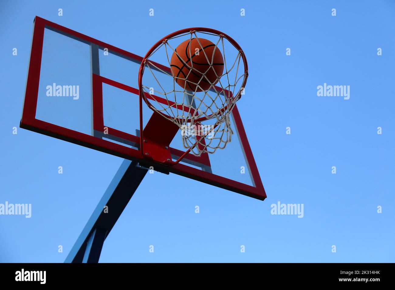 Ein Basketballball fliegt in einen Korb auf einem Straßenbasketballplatz. Ein Basketballspiel. Der Ball gegen den Himmel im Tor. Stockfoto