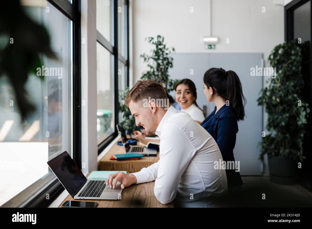 Geschäftsmann, der am Arbeitsplatz von Kollegen am Laptop arbeitet Stockfoto