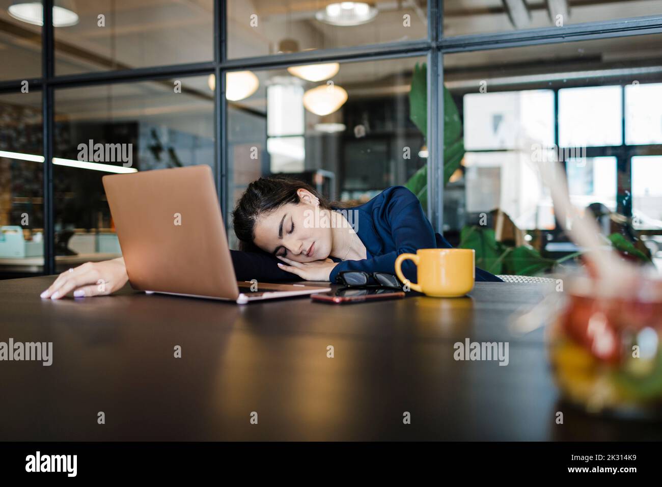 Müde Geschäftsfrau mit Laptop, die im Büro ein Nickerchen macht Stockfoto