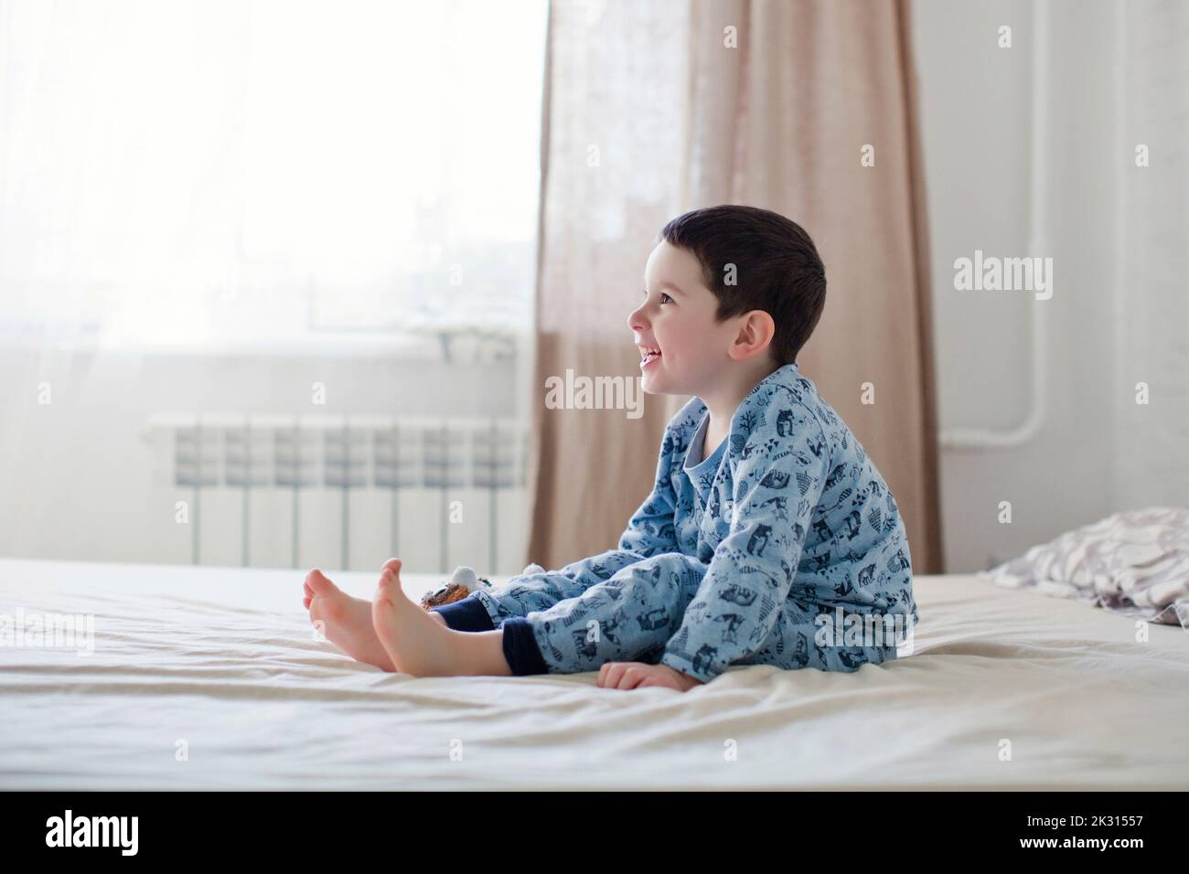 Fröhlicher Junge im Schlafanzug, der auf dem Bett sitzt Stockfoto