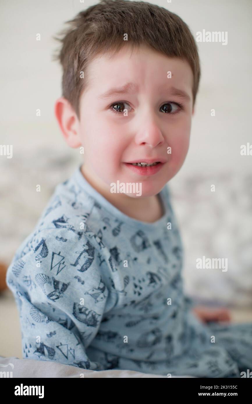 Weinender Junge im Schlafanzug auf dem Bett Stockfoto