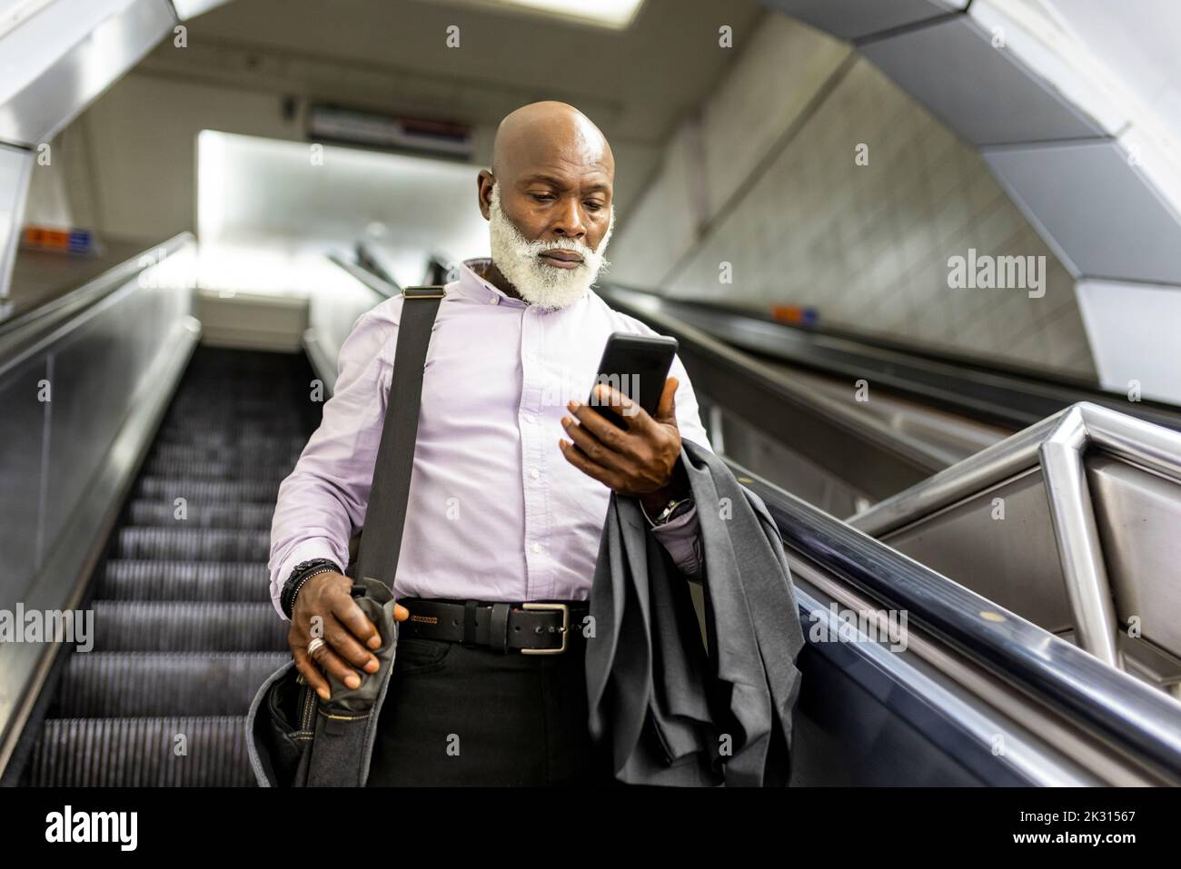 Senior Pendler mit Laptoptasche mit Smartphone auf Rolltreppe Stockfoto