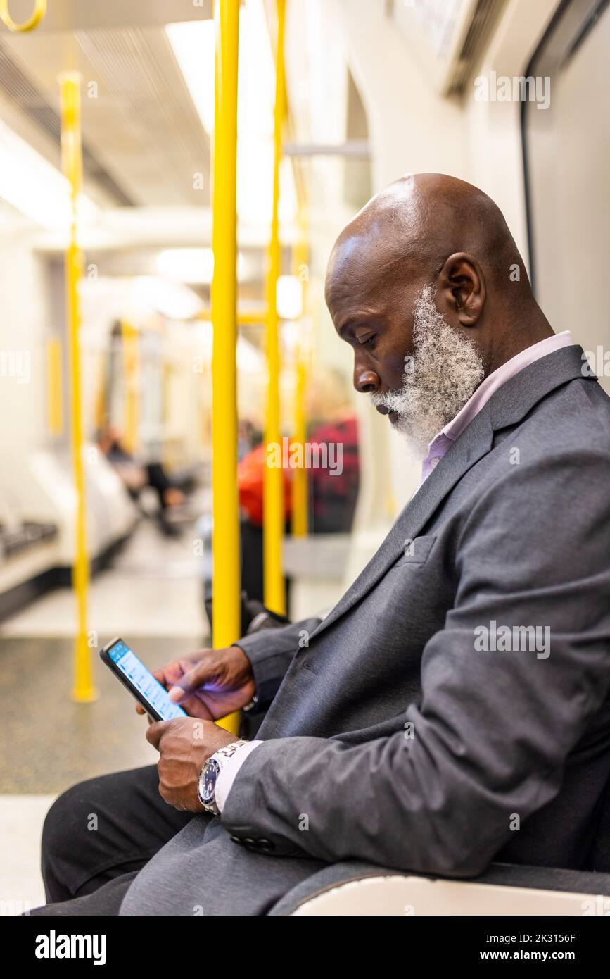 Kahlköpfiger Geschäftsmann, der im U-Bahn-Zug ein Mobiltelefon benutzt Stockfoto
