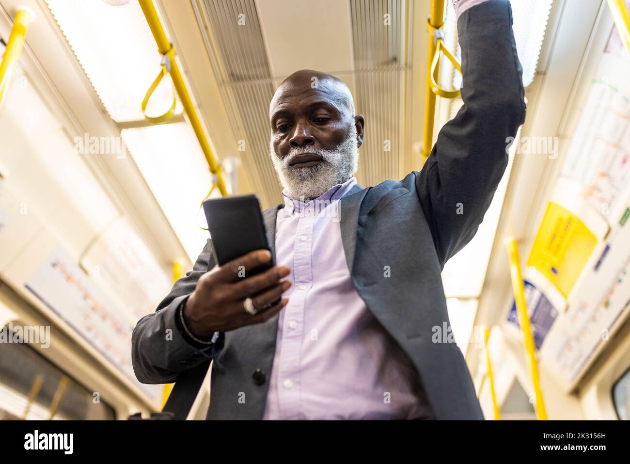 Leitender Geschäftsmann, der im U-Bahn-Zug ein Mobiltelefon benutzt Stockfoto