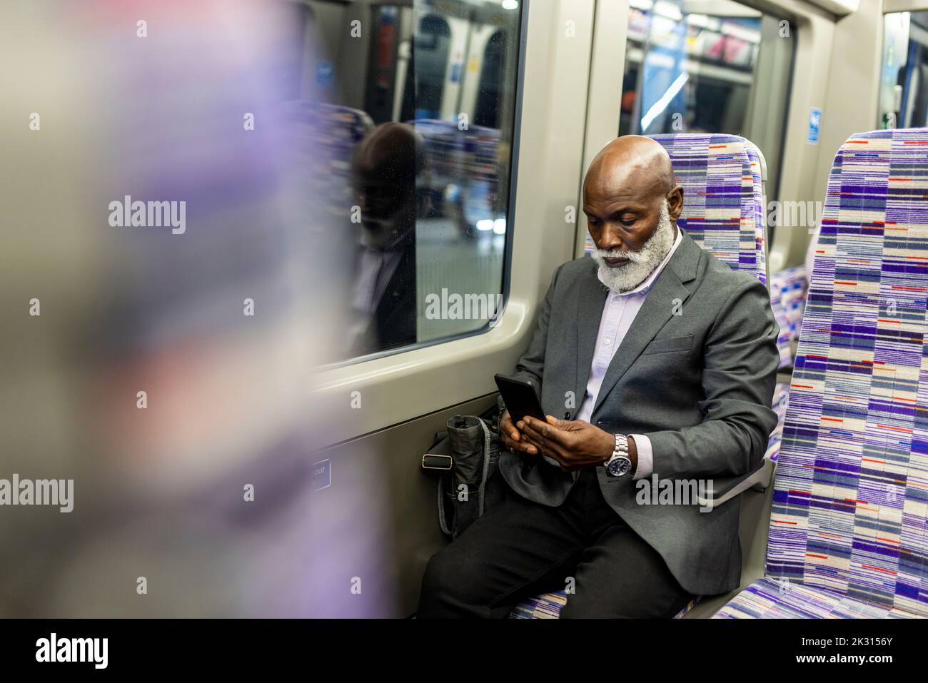 Leitender Geschäftsmann, der im Zug ein Mobiltelefon verwendet Stockfoto