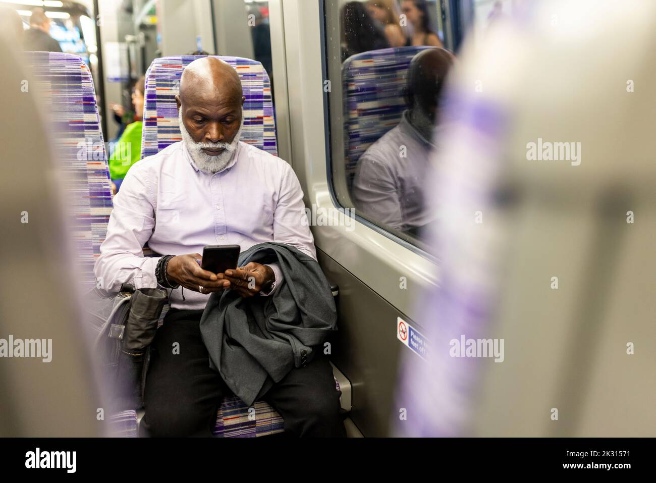 Kahlköpfiger Geschäftsmann, der im Zug ein Mobiltelefon verwendet Stockfoto
