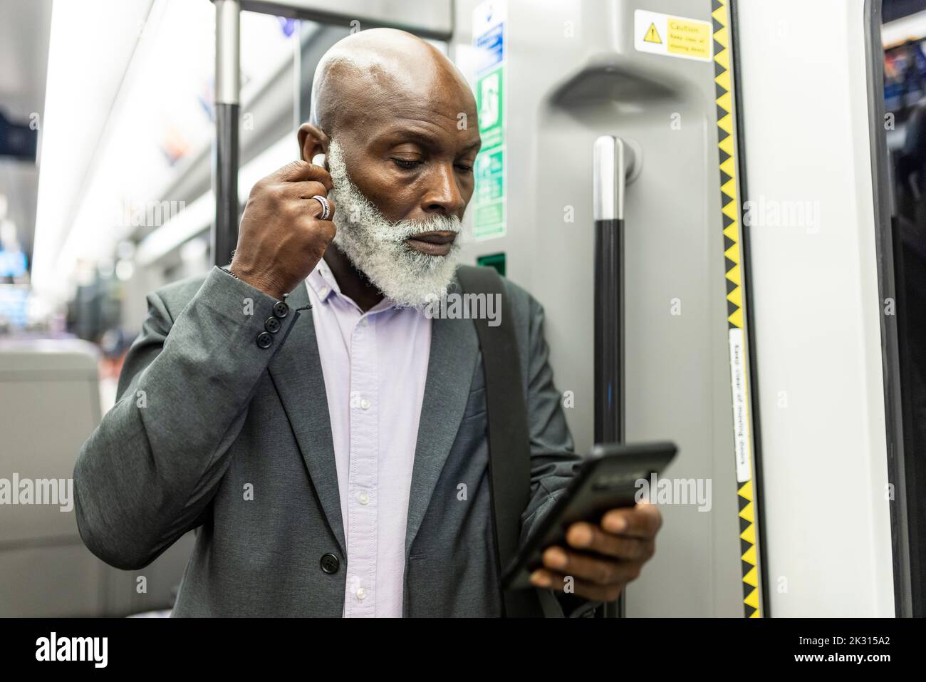 Leitender Geschäftsmann, der im Zug ein Smartphone verwendet und kabellose in-Ear-Kopfhörer anpasst Stockfoto