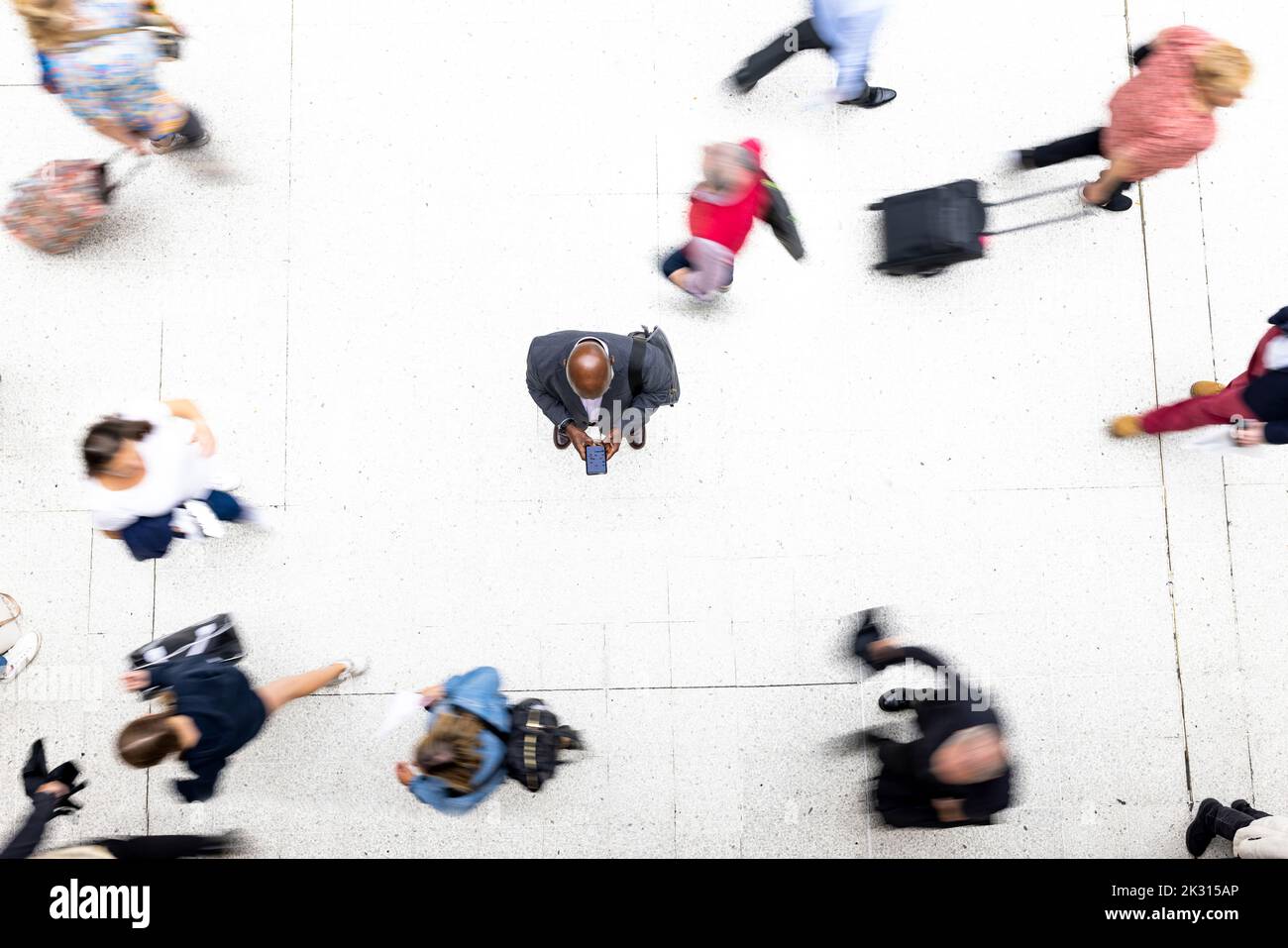 Geschäftsmann mit Mobiltelefon, umgeben von Pendlern am Bahnhof Stockfoto
