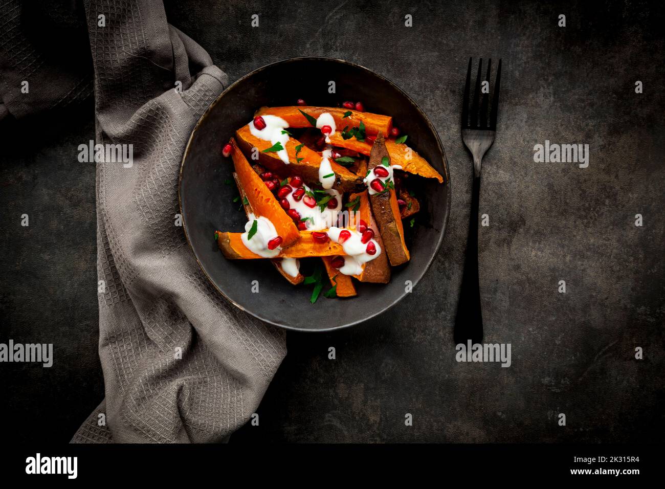 Studioaufnahme einer Schüssel mit Süßkartoffeln mit Petersilie, Granatapfelkernen und Joghurtsauce Stockfoto