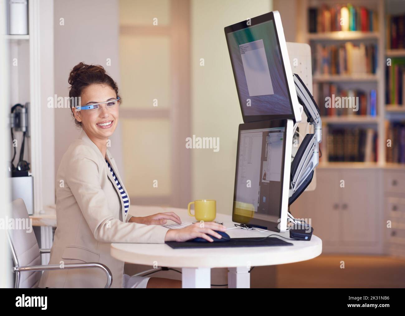 Meine Brille macht das Geschäft tragbar. Porträt einer jungen Frau, die eine intelligente Brille trägt, während sie an einem Computer mit zwei Bildschirmen arbeitet. Stockfoto