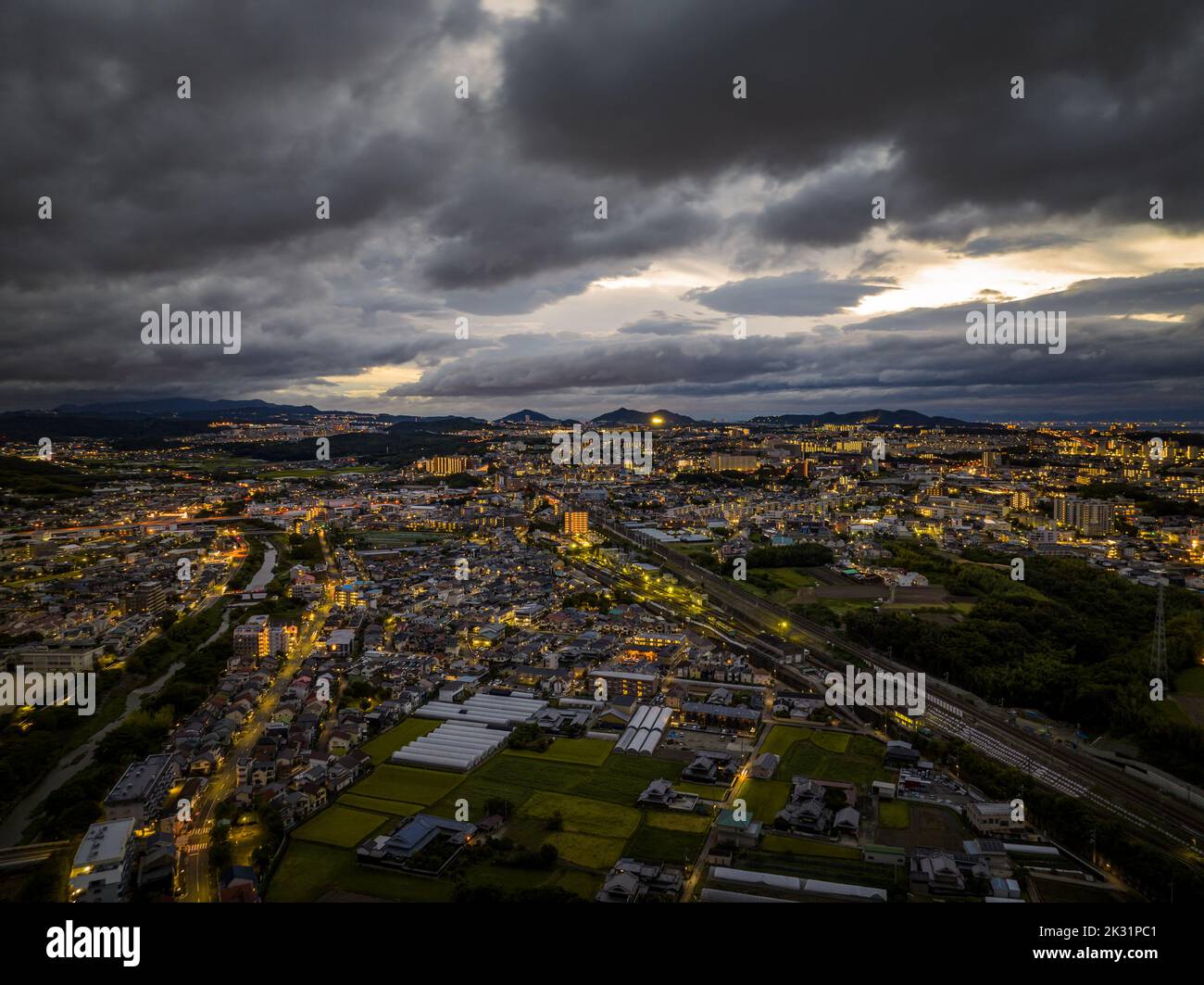 Luftaufnahme von dramatischen Sturmwolken über ausgedehnten Stadtlichtern bei Sonnenaufgang Stockfoto
