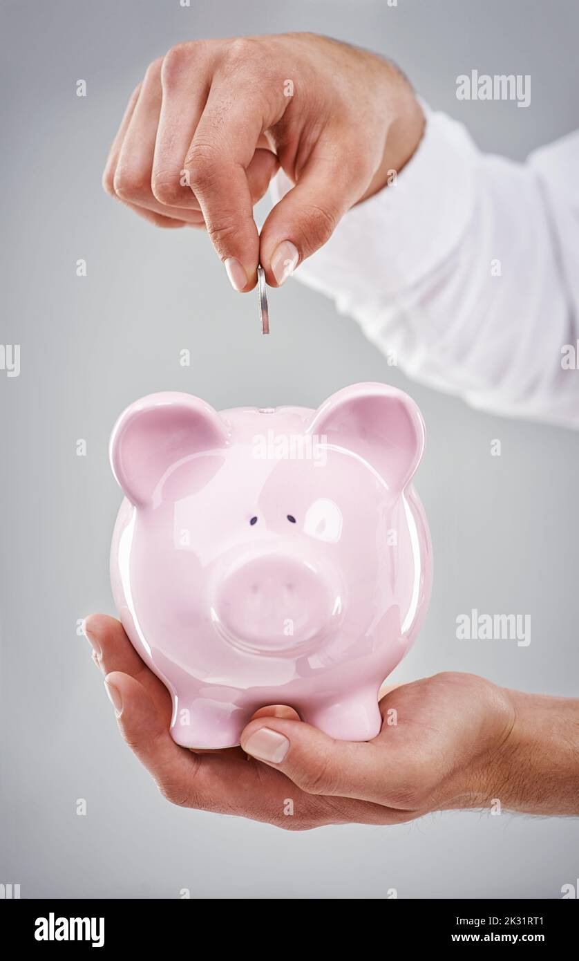 Jeden Cent sparen. Zugeschnittenes Bild eines Mannes, der Geld in ein Sparschwein gesteckt hat. Stockfoto