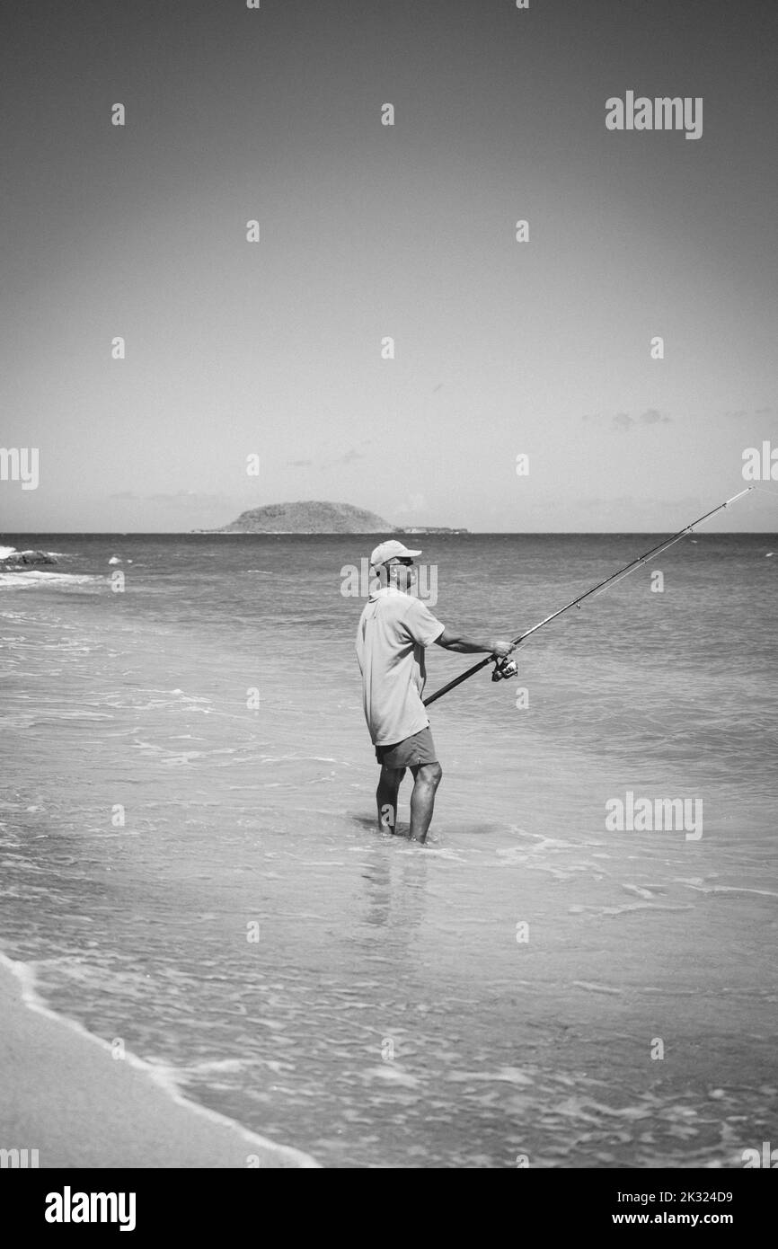 Eine vertikale Schwarzweißaufnahme eines Fischers am Strand von Guadeloupe bei Tageslicht Stockfoto