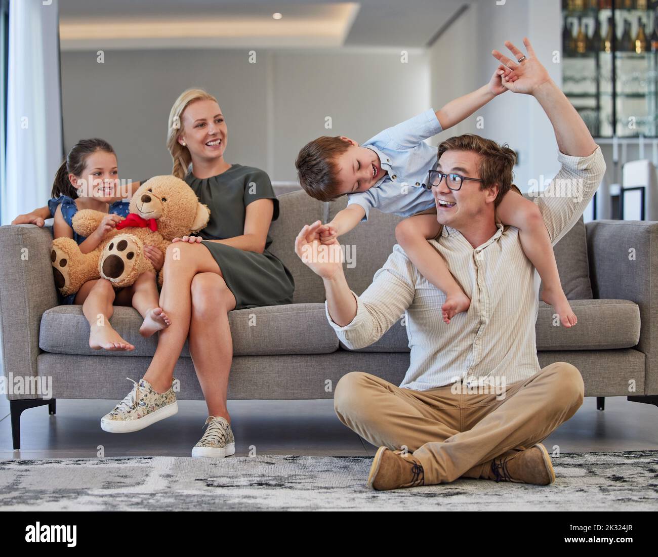Glückliche Familie, spielende Kinder und fürsorgliche Eltern, die Spaß haben, während sie sich verbinden, lieben und zusammen in der Lounge zu Hause sitzen. Mann, Frau und Kinder Stockfoto