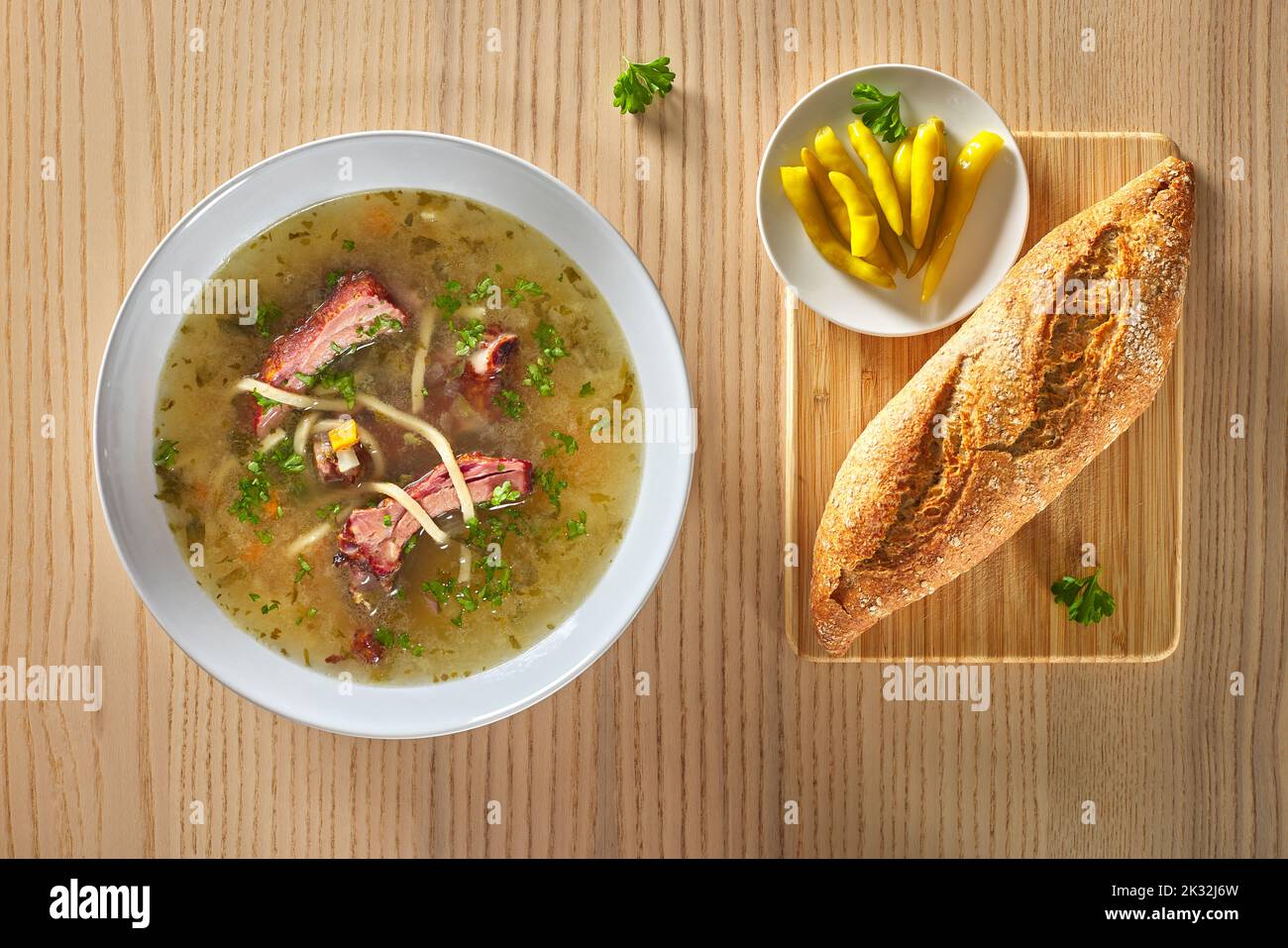 Suppe aus geräucherten Rippchen mit Gemüse, Brot, eingelegten Chilischoten und Kräutern in einer weißen Schüssel, die auf Holzboden steht Stockfoto
