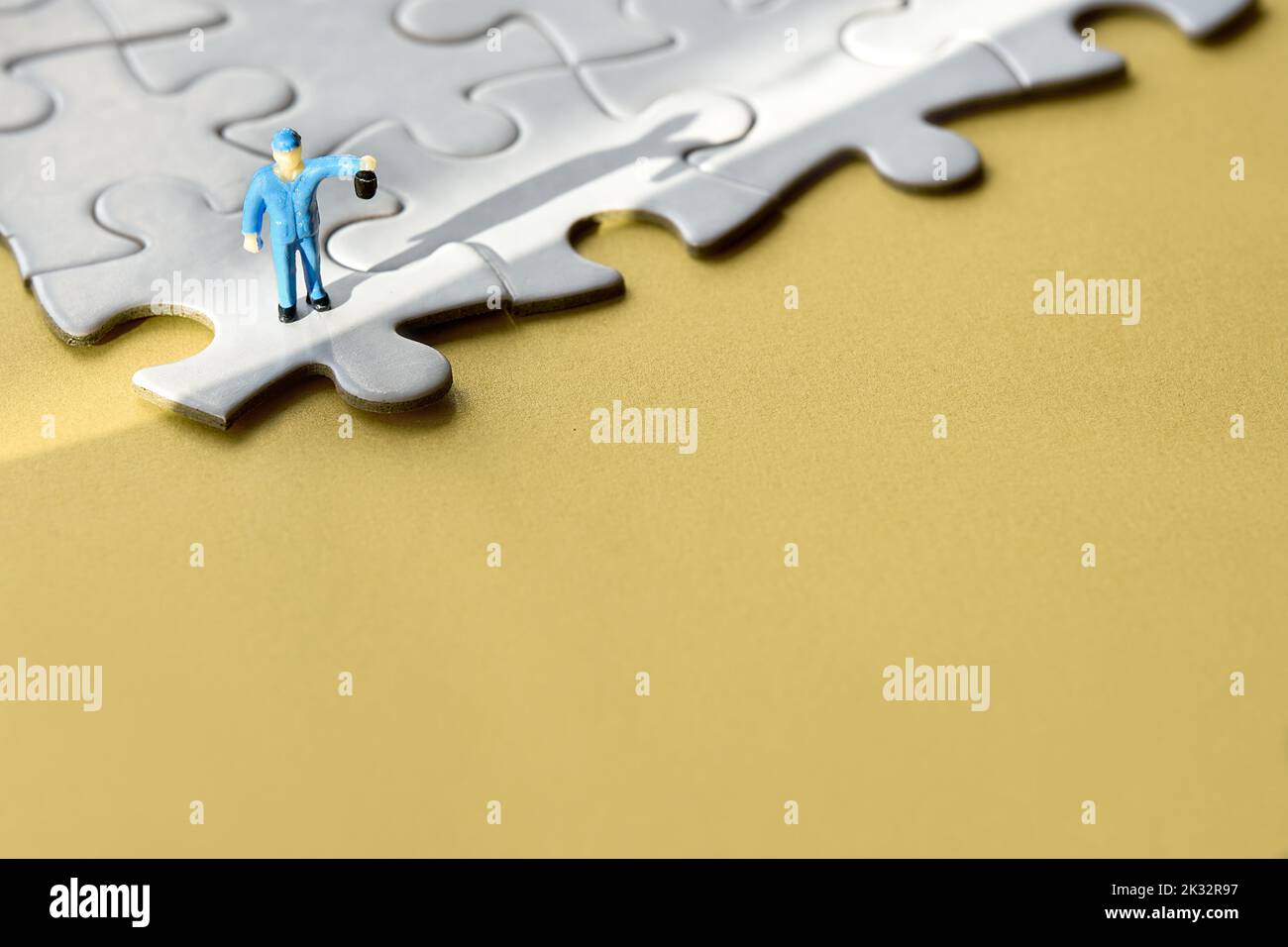 Einzelne kleine Arbeiter Miniatur-Figur am Rand des verbundenen Puzzle. Gelber Papierhintergrund, langer Schatten. Konzept Hintergrund mit Copy-Space, Ort Stockfoto