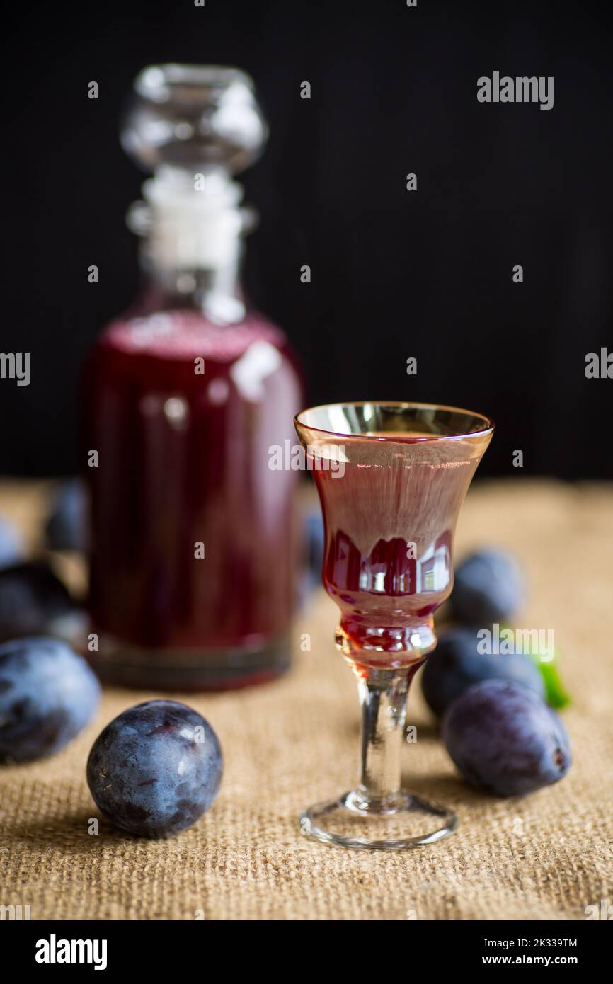 Pflaumenroter Wein in einem Glas und ein Dekanter vor dem Hintergrund von reifen großen Pflaumen auf dem Tisch. Stockfoto