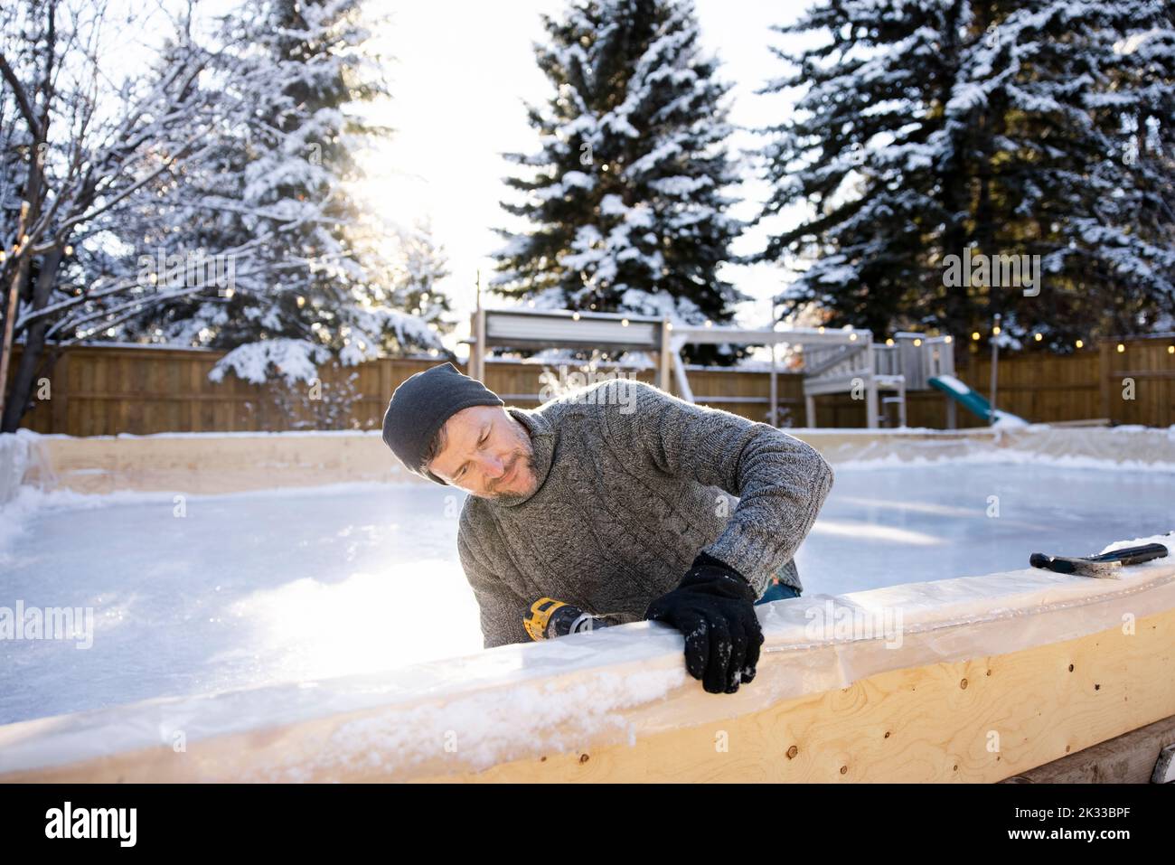 Mann mit Bohrmaschine beim Bau einer Eisbahn im verschneiten Hinterhof Stockfoto